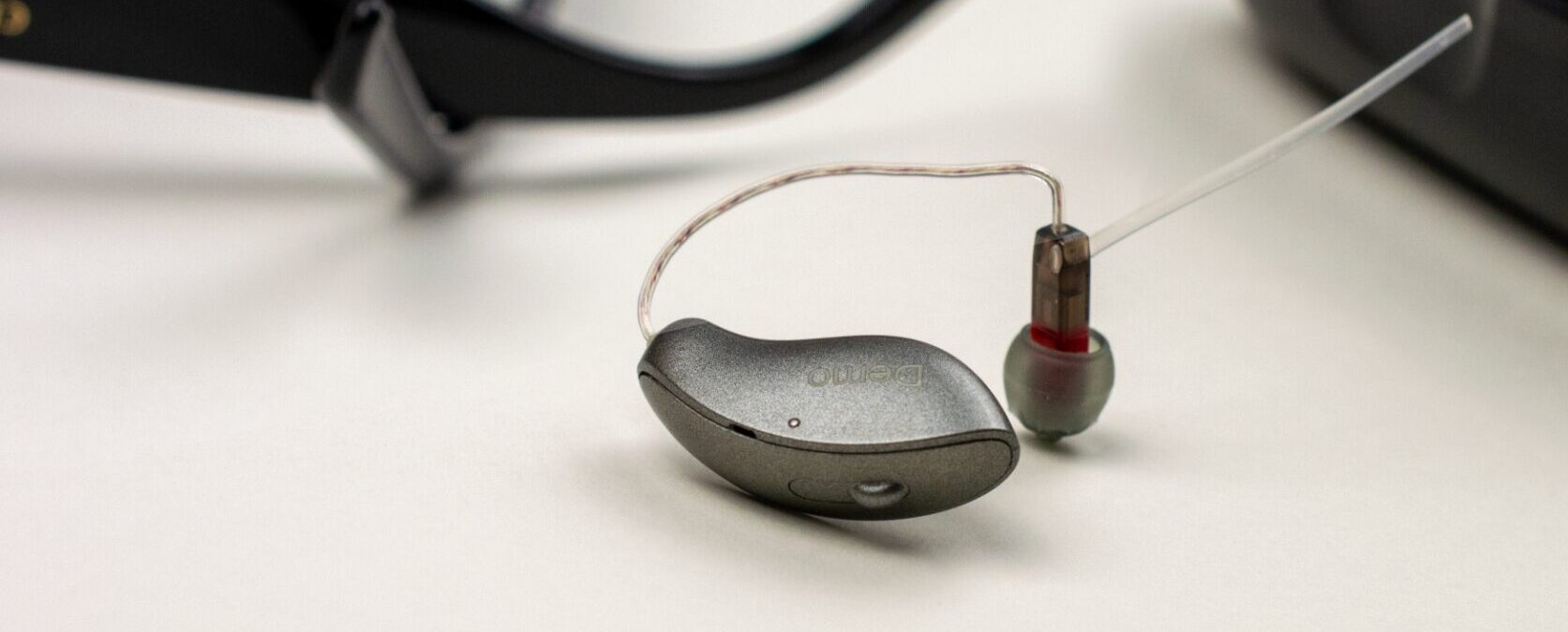 Hearing aid on a table with glasses frames in the background